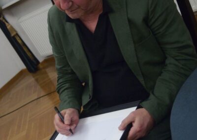 Janusz L. Wisniewski podpisujący się na białej planszy.
